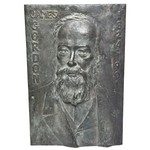 fig 2. A rectangular dark bronze bas-relief plaque displaying a portrait of a bearded man with raised lettering and an incised signature.