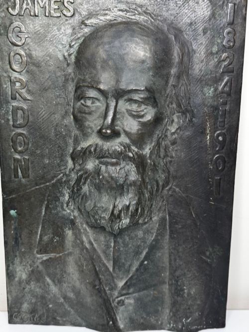 fig 3. A rectangular dark bronze bas-relief plaque displaying a portrait of a bearded man with raised lettering and an incised signature.