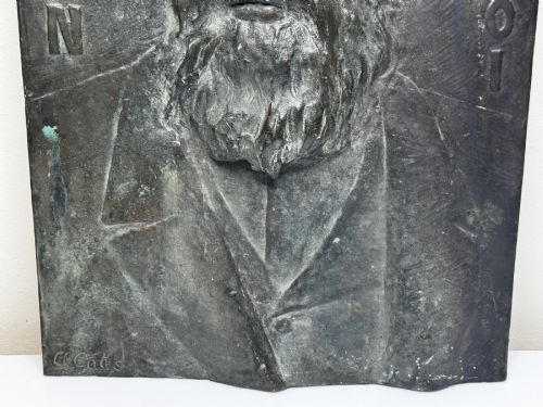 fig 4. A rectangular dark bronze bas-relief plaque displaying a portrait of a bearded man with raised lettering and an incised signature.
