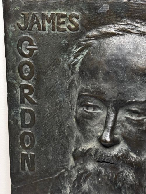 fig 5. A rectangular dark bronze bas-relief plaque displaying a portrait of a bearded man with raised lettering and an incised signature.