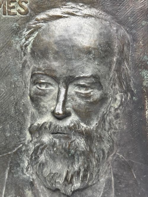 fig 6. A rectangular dark bronze bas-relief plaque displaying a portrait of a bearded man with raised lettering and an incised signature.