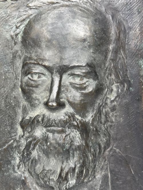 fig 7. A rectangular dark bronze bas-relief plaque displaying a portrait of a bearded man with raised lettering and an incised signature.