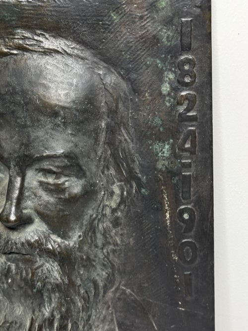 fig 8. A rectangular dark bronze bas-relief plaque displaying a portrait of a bearded man with raised lettering and an incised signature.