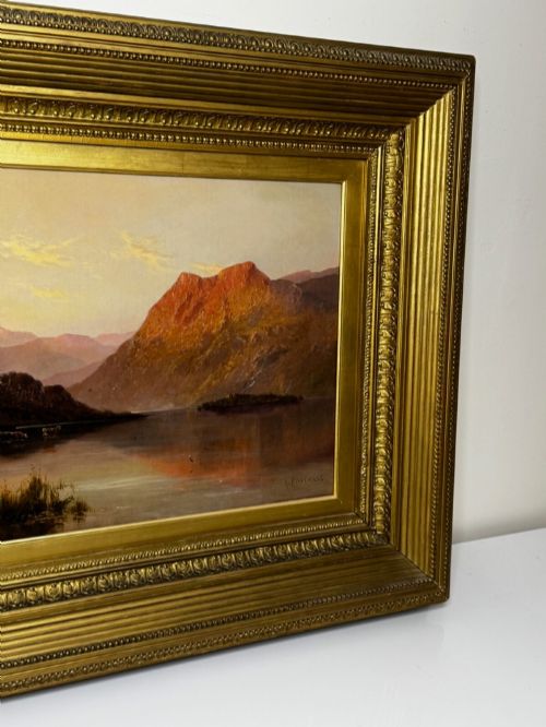fig 6. An antique oil painting depicting a lake surrounded by mountains at sunset, enclosed within a carved gold frame.