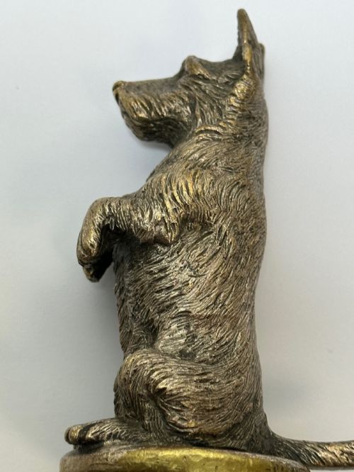 fig 7. A cast bronze car mascot depicting a Scottish Terrier sitting in a begging pose mounted on a small circular base with a threaded bolt.