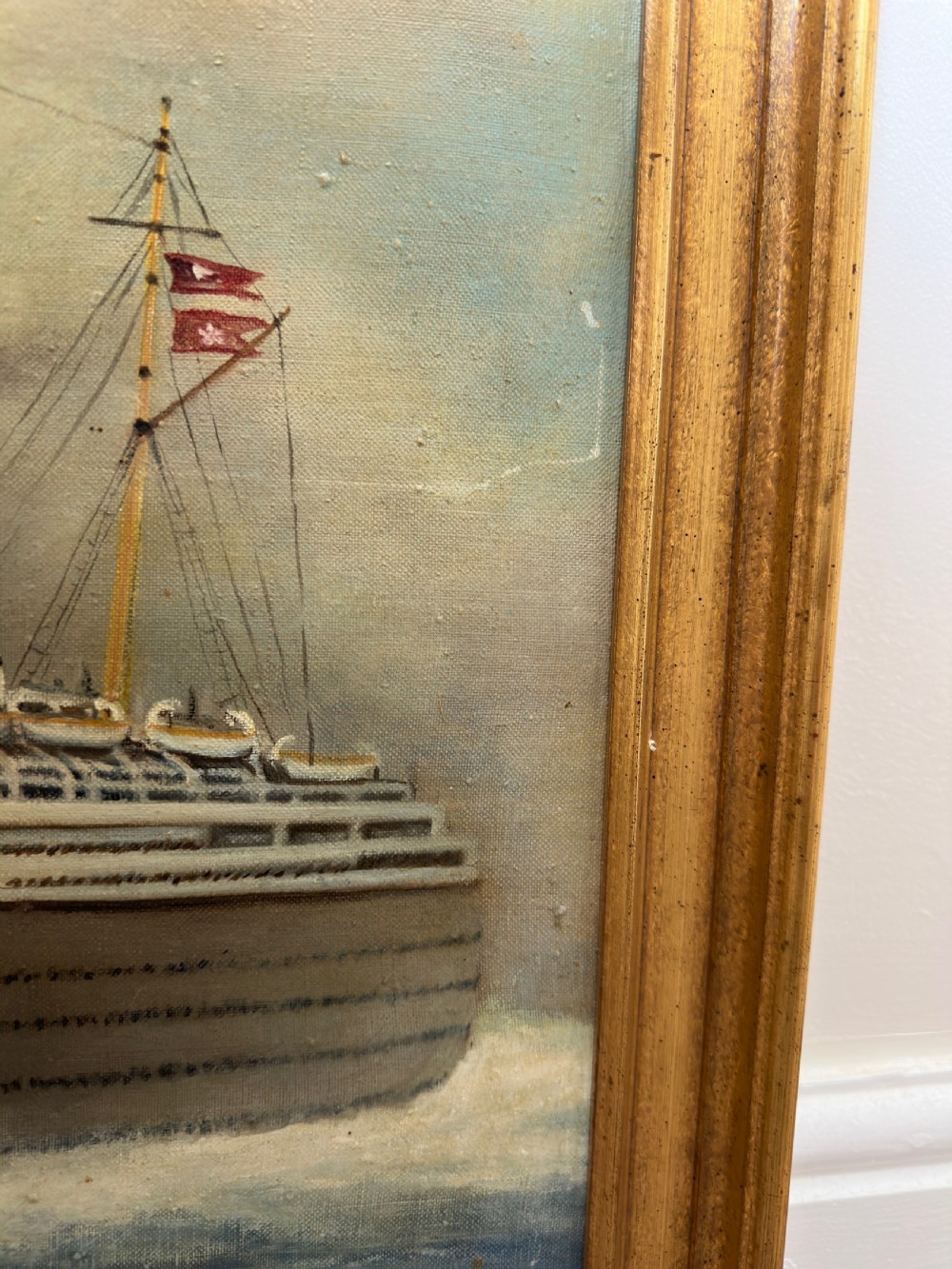 An oil painting depicting the RMS Queen Mary ocean liner sailing across blue waters under a cloudy sky, framed in a moulded gold gilt border. View VII