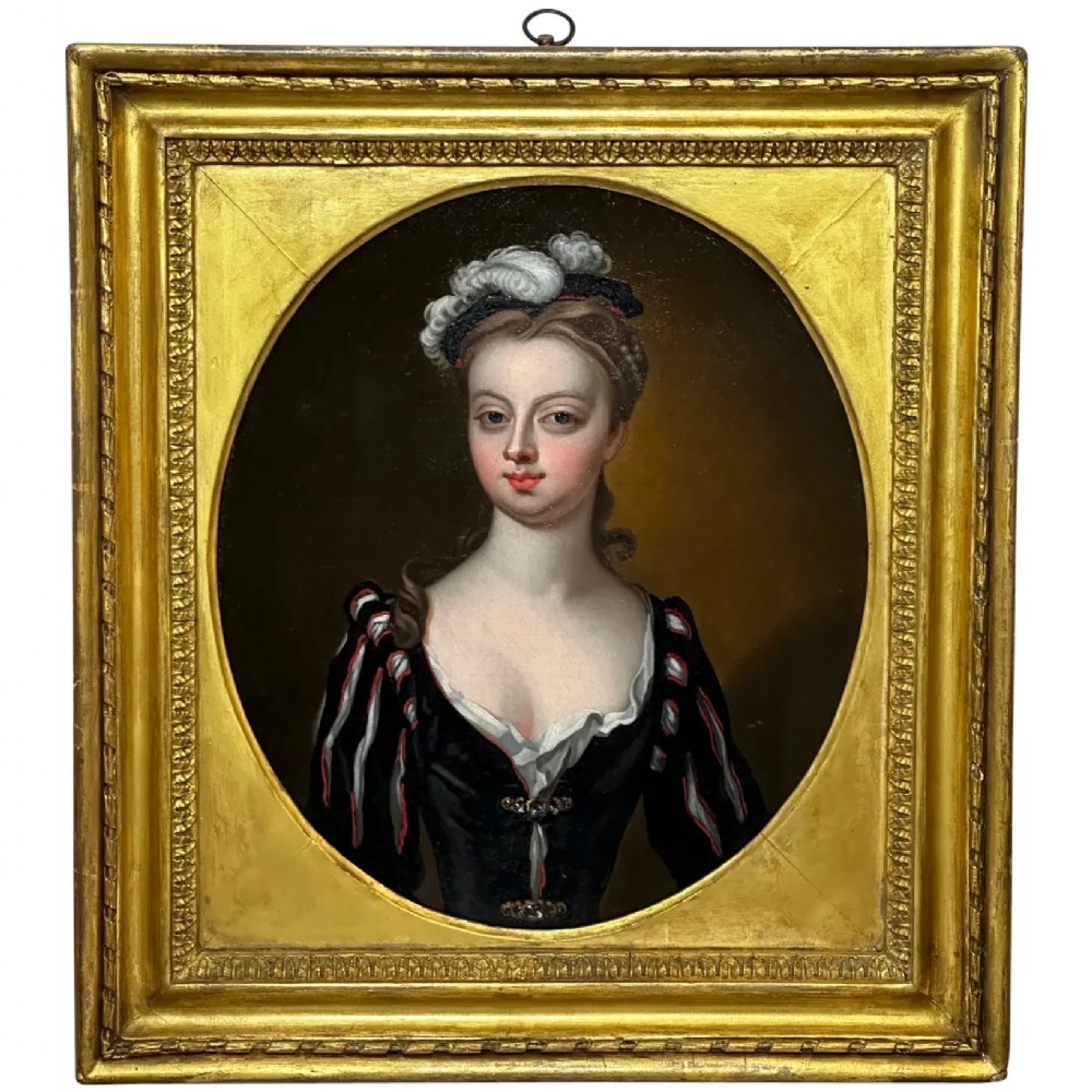 An 18th-century oil portrait of a lady in a black bodice and feathered headpiece within an oval spandrel inside a square gilded frame.