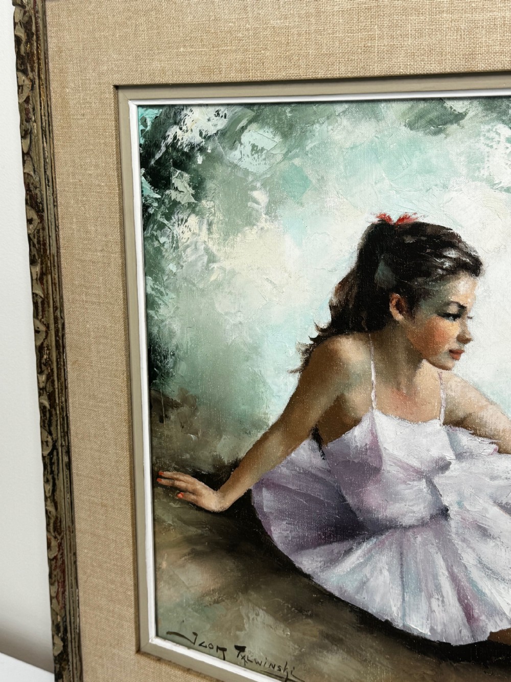 A framed mid-century oil painting depicting a seated ballerina in a white tutu holding a small bouquet of flowers against a textured soft green background. View IV