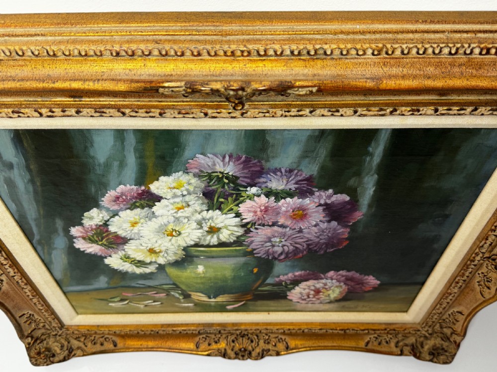 A framed Victorian oil painting depicting a bouquet of pink and white chrysanthemums in a green glazed ceramic vase set against a dark background, encased in an ornate gilded frame. View VII