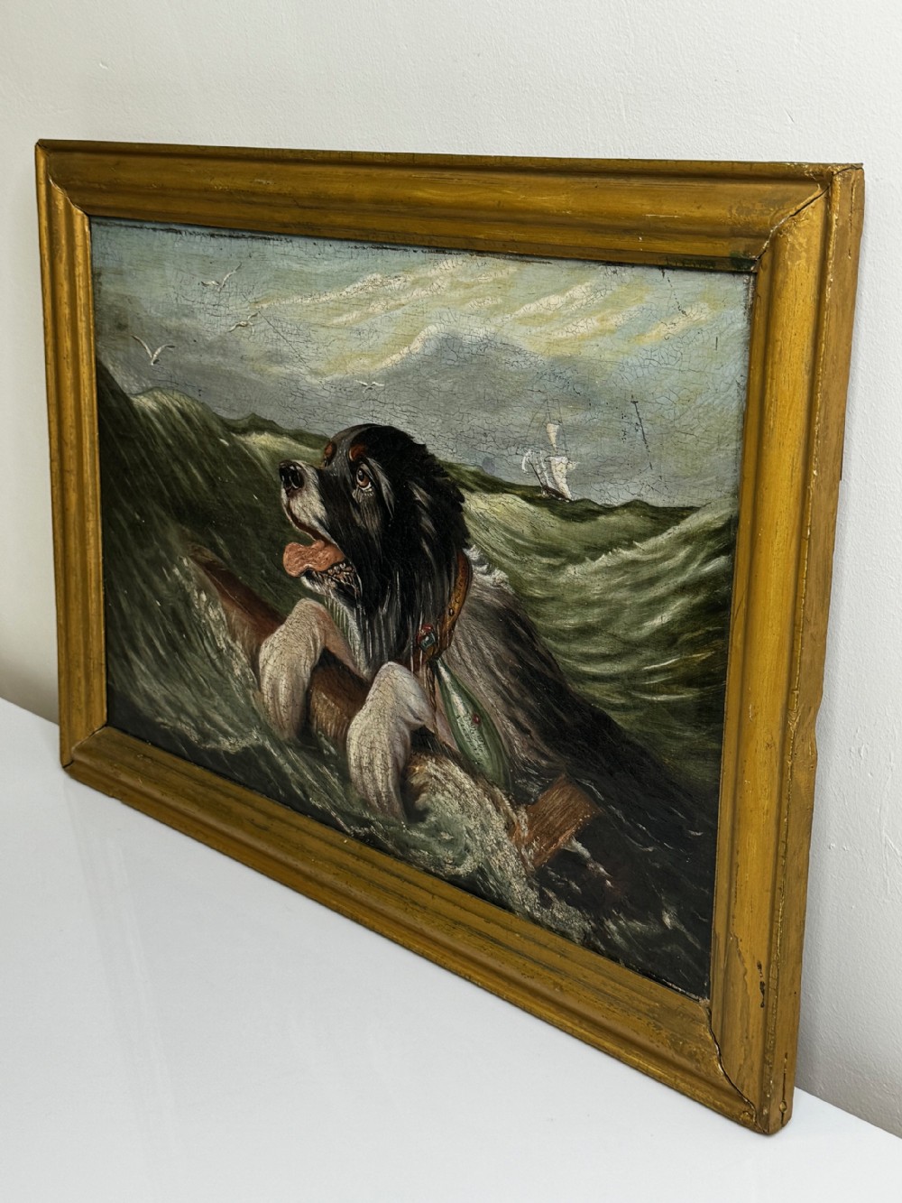 An antique oil painting depicting a Saint Bernard dog swimming in sea waves while clinging to a wooden spar, set within a gilded wooden frame. View X
