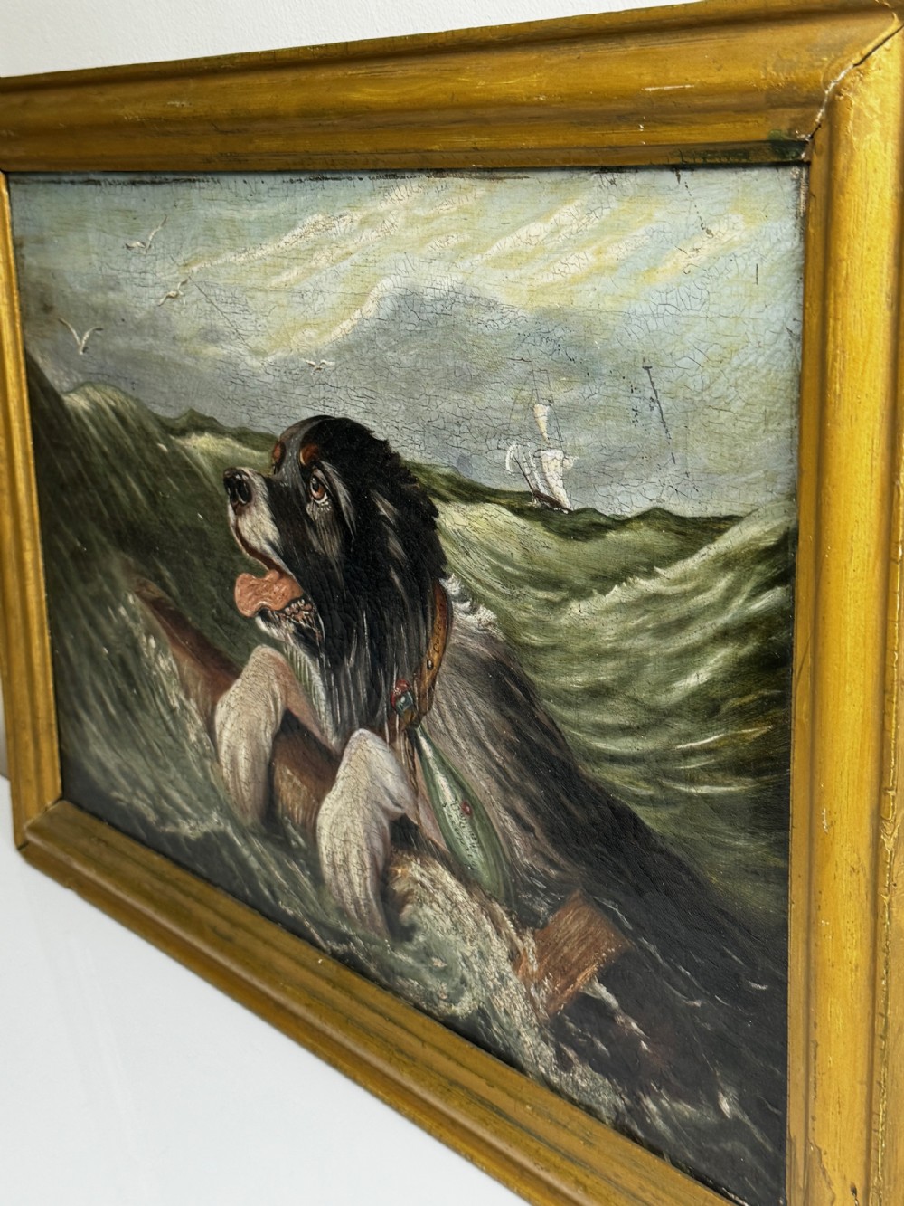 An antique oil painting depicting a Saint Bernard dog swimming in sea waves while clinging to a wooden spar, set within a gilded wooden frame. View XI