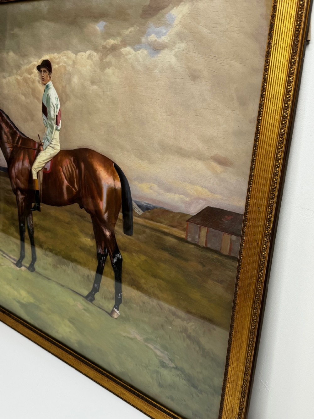 A nineteenth-century oil painting depicting a brown thoroughbred horse with a jockey in white and red silks, framed in a ribbed gold-leaf frame. View IX
