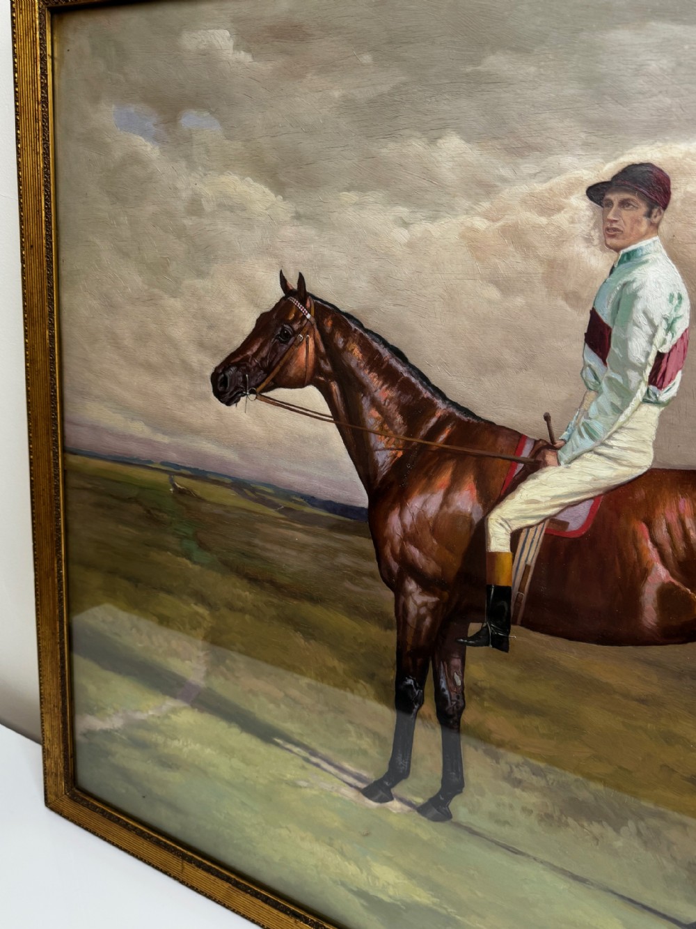 A nineteenth-century oil painting depicting a brown thoroughbred horse with a jockey in white and red silks, framed in a ribbed gold-leaf frame. View XVI