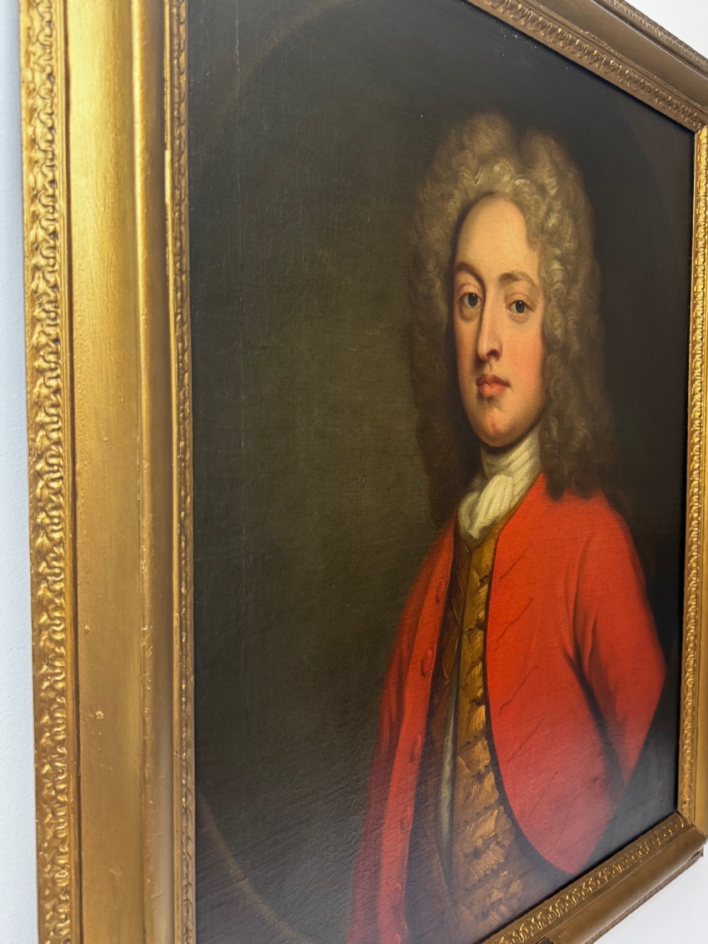 An 18th-century oil portrait painting depicting a gentleman in a red coat and white cravat housed within a moulded giltwood frame. View II