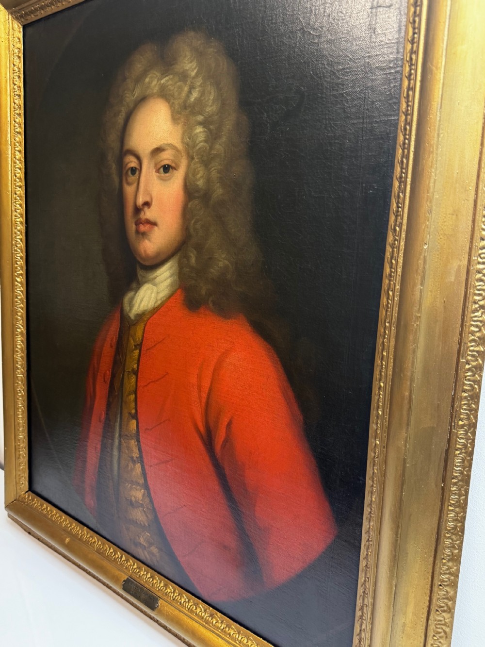 An 18th-century oil portrait painting depicting a gentleman in a red coat and white cravat housed within a moulded giltwood frame. View III