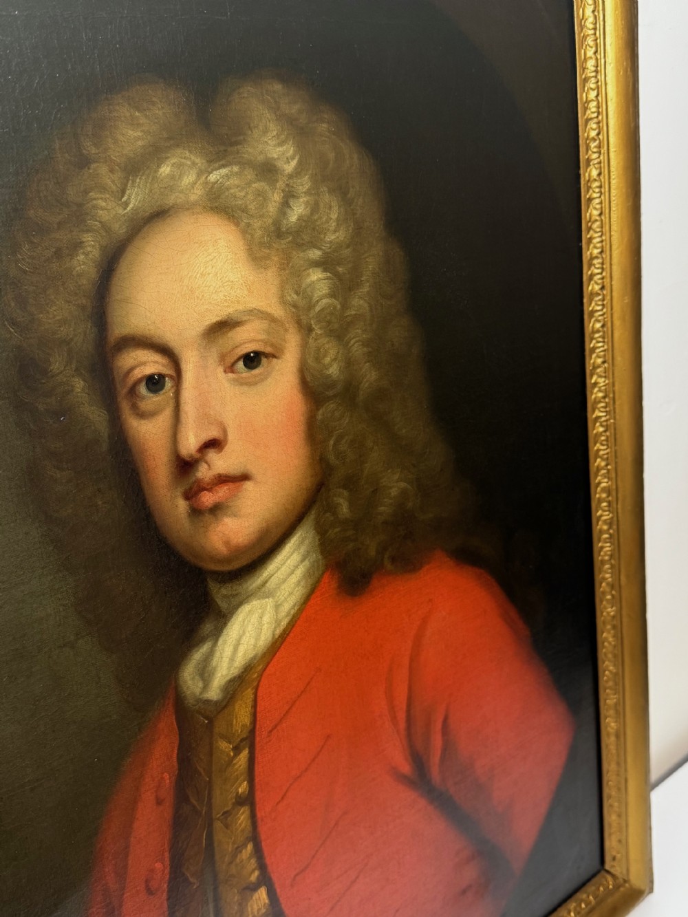 An 18th-century oil portrait painting depicting a gentleman in a red coat and white cravat housed within a moulded giltwood frame. View IX