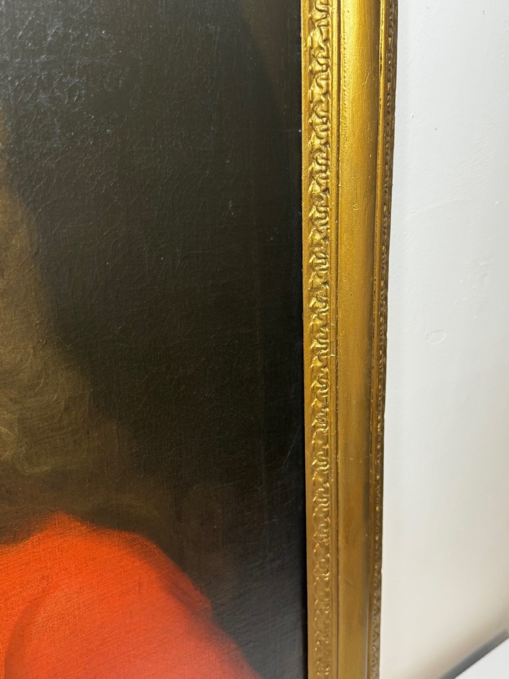 An 18th-century oil portrait painting depicting a gentleman in a red coat and white cravat housed within a moulded giltwood frame. View X