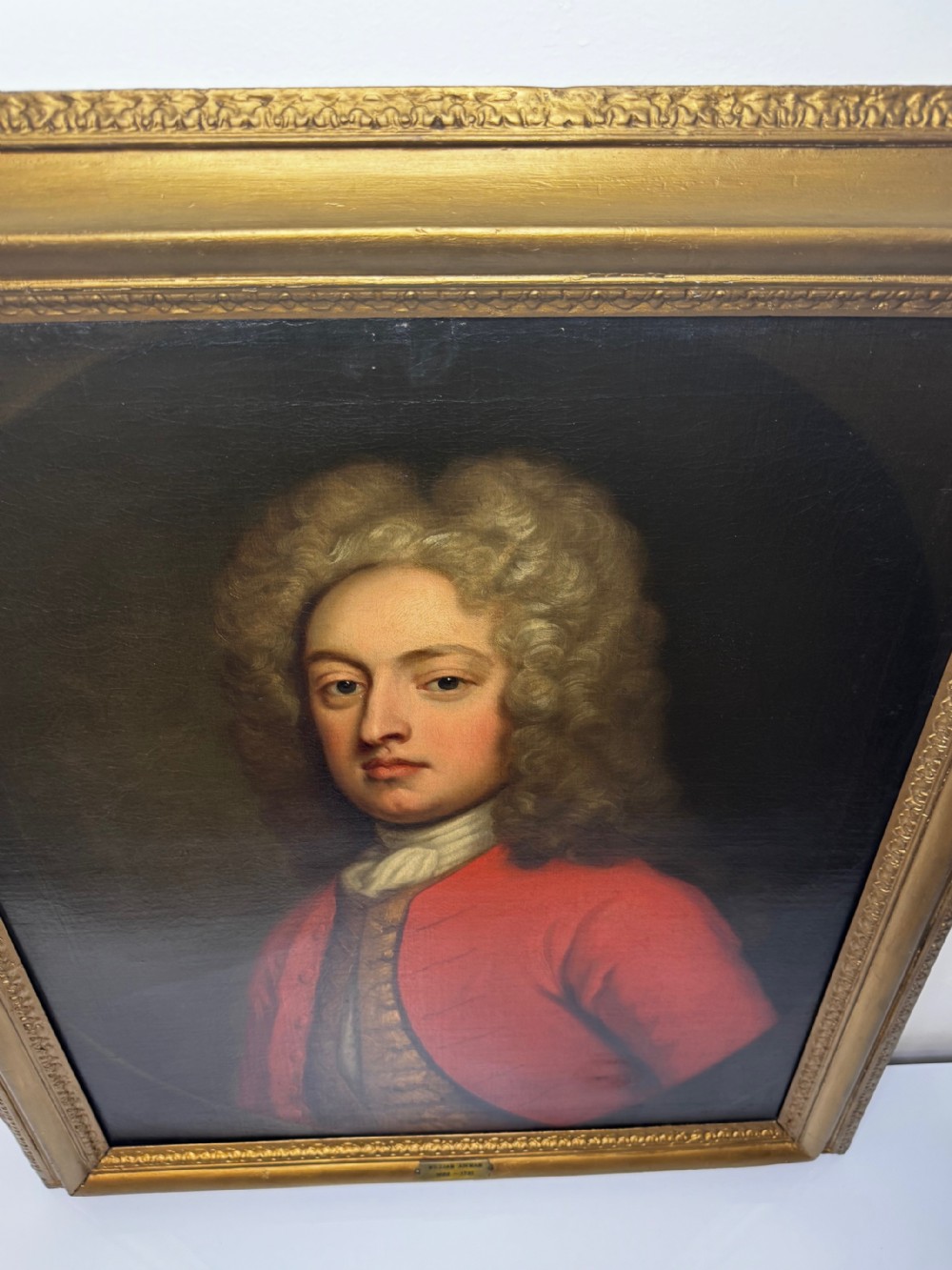An 18th-century oil portrait painting depicting a gentleman in a red coat and white cravat housed within a moulded giltwood frame. View XI