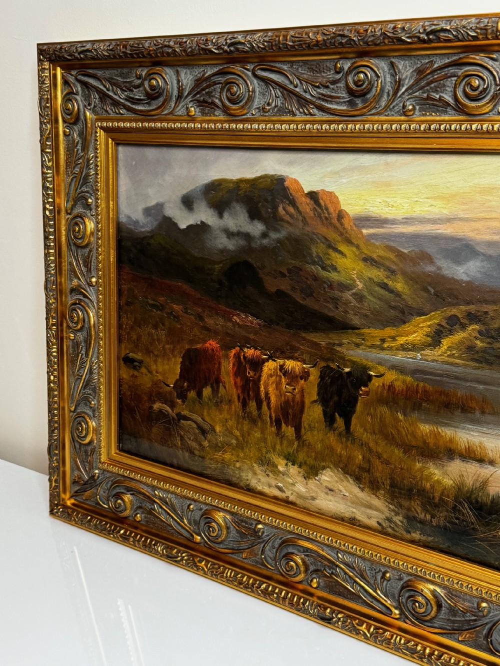 A Victorian oil painting depicting Highland cattle beside a loch against a mountainous backdrop, set within an ornate gilded frame. View IV