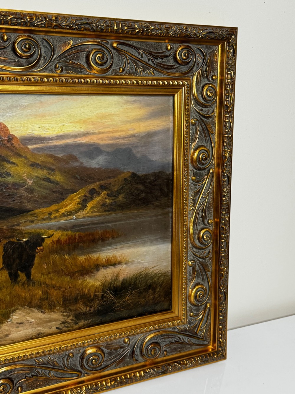 A Victorian oil painting depicting Highland cattle beside a loch against a mountainous backdrop, set within an ornate gilded frame. View VI