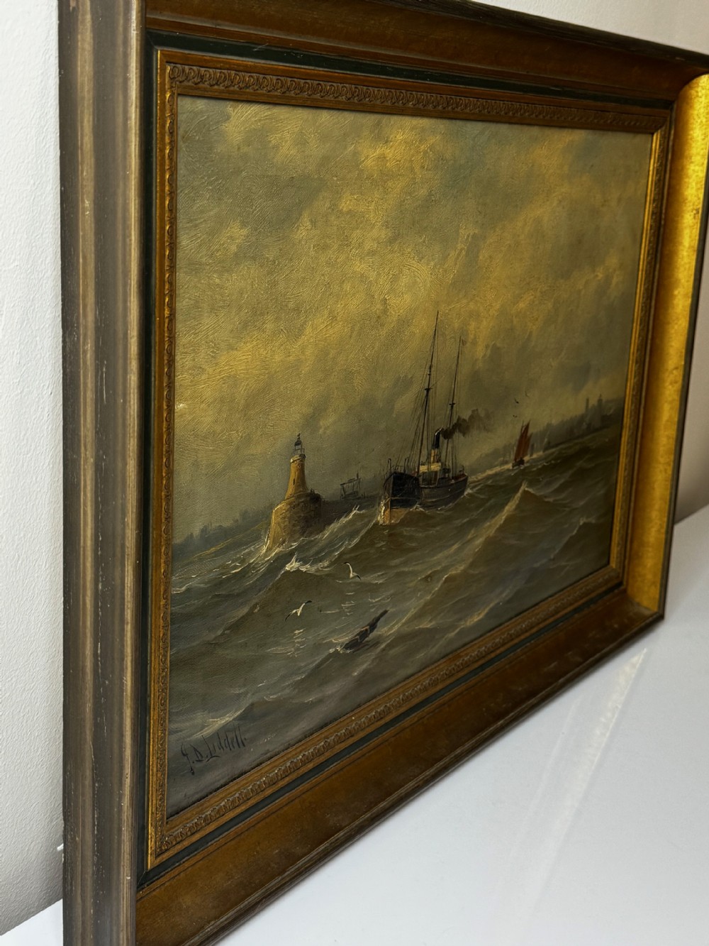 An antique framed oil painting depicting a steam pilot boat navigating choppy grey waters near a lighthouse under an overcast sky. View XXIII