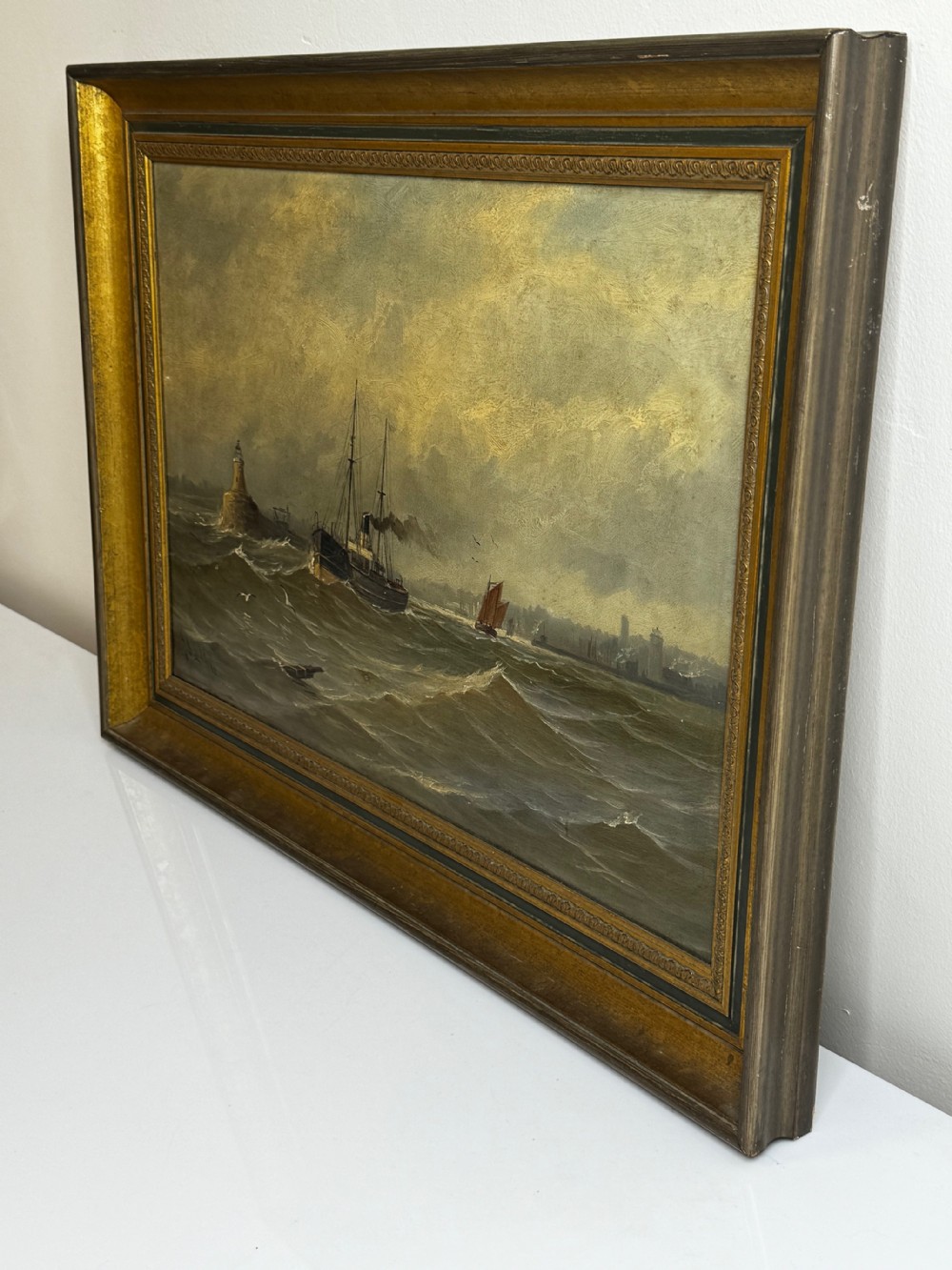 An antique framed oil painting depicting a steam pilot boat navigating choppy grey waters near a lighthouse under an overcast sky. View XXIV