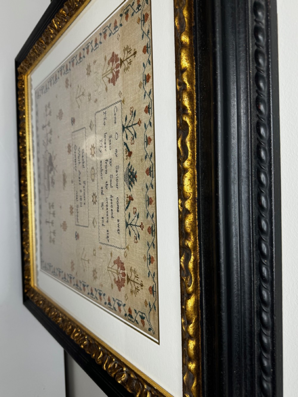 A framed 1831 needlework sampler featuring embroidered religious verse, floral borders, and a central stag motif on a linen background. View III