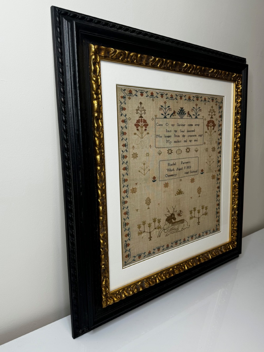 A framed 1831 needlework sampler featuring embroidered religious verse, floral borders, and a central stag motif on a linen background. View VIII