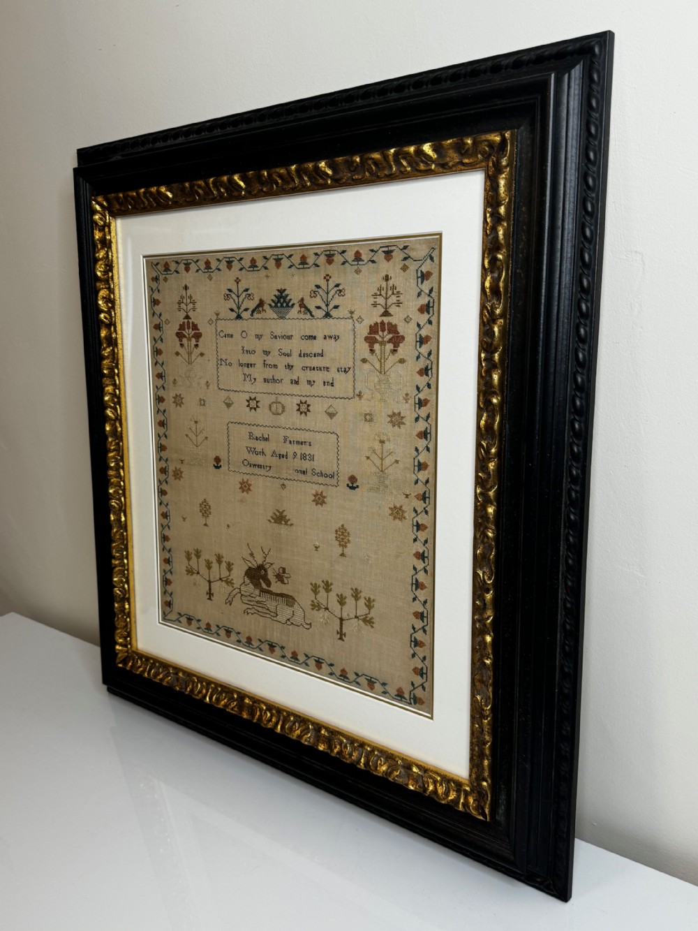 A framed 1831 needlework sampler featuring embroidered religious verse, floral borders, and a central stag motif on a linen background. View IX
