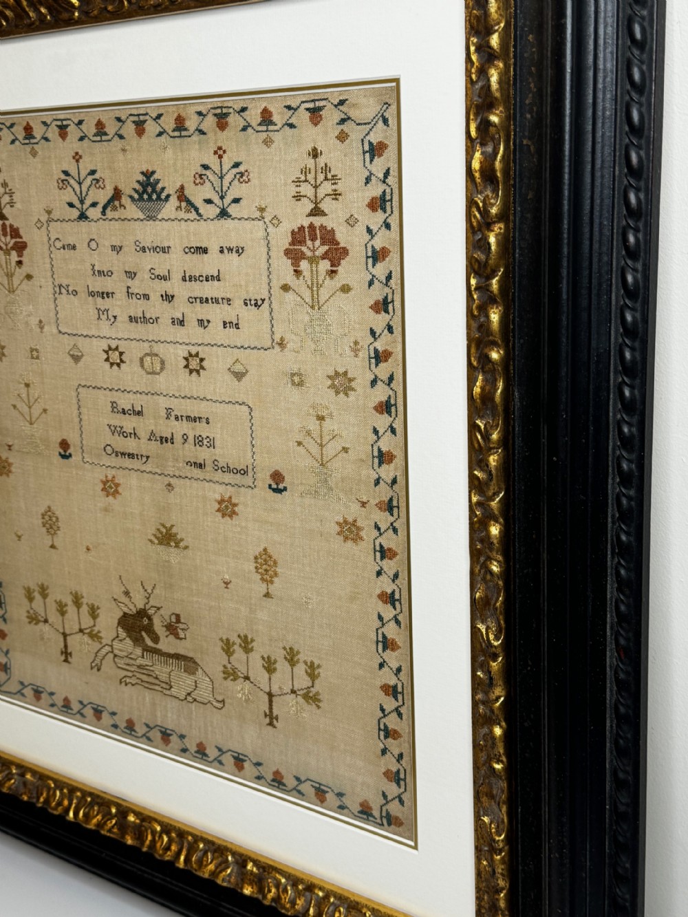 A framed 1831 needlework sampler featuring embroidered religious verse, floral borders, and a central stag motif on a linen background. View X