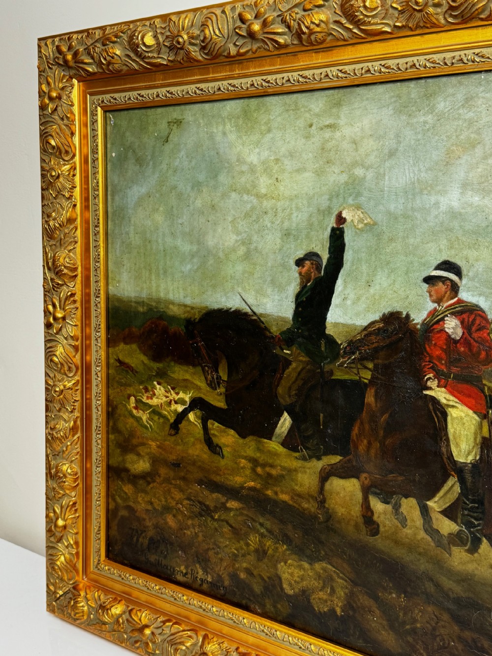 An antique oil painting depicting huntsmen riding horses alongside hounds in an open landscape, housed within an ornate carved gold gilt frame. View III