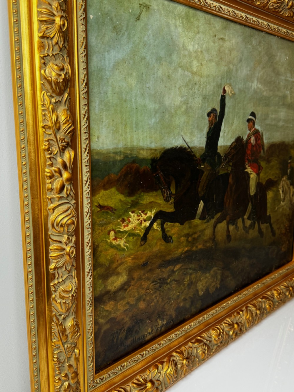 An antique oil painting depicting huntsmen riding horses alongside hounds in an open landscape, housed within an ornate carved gold gilt frame. View VII