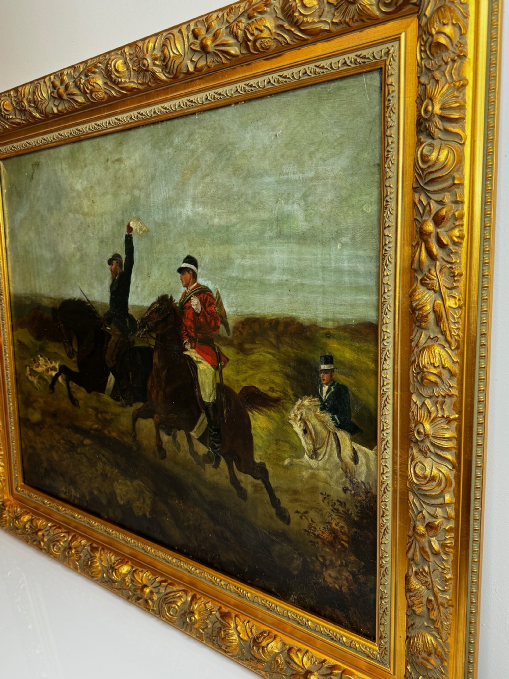 An antique oil painting depicting huntsmen riding horses alongside hounds in an open landscape, housed within an ornate carved gold gilt frame. View IX