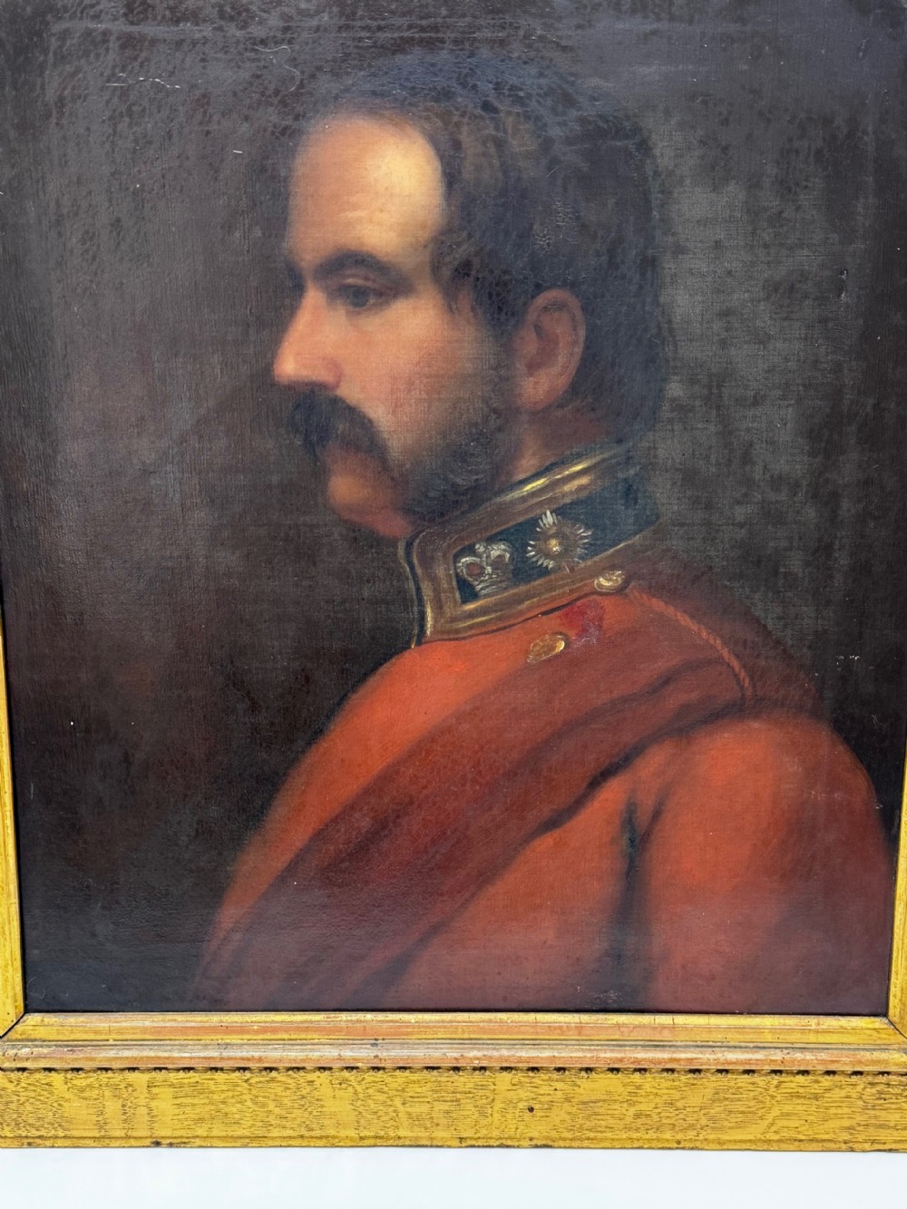 A profile view Victorian oil painting depicting a military officer with a moustache in a red uniform coat, set within a gilded wooden frame. View V