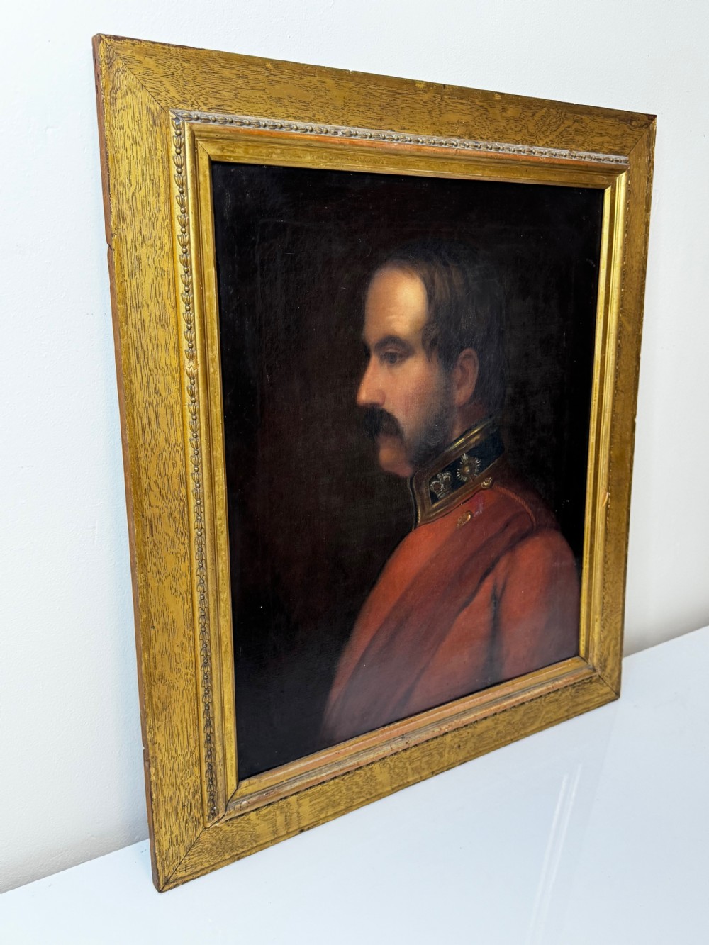 A profile view Victorian oil painting depicting a military officer with a moustache in a red uniform coat, set within a gilded wooden frame. View VIII