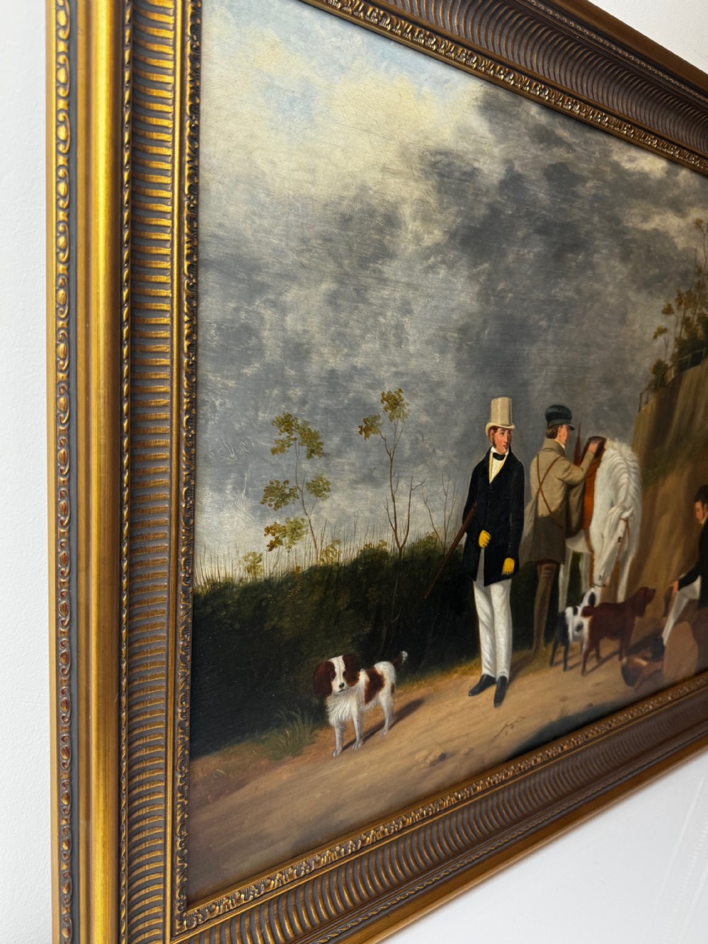 An antique oil painting in a decorative gilded frame depicting three men with hunting dogs and a white horse in a countryside setting. View IX