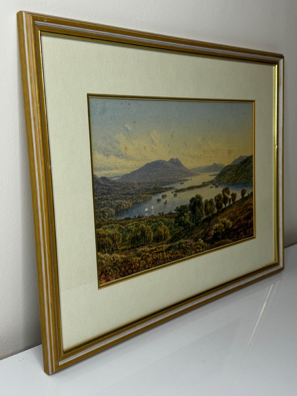 A framed Edwardian watercolour painting depicting an elevated landscape view over Lake Windermere surrounded by hills and trees. View IX