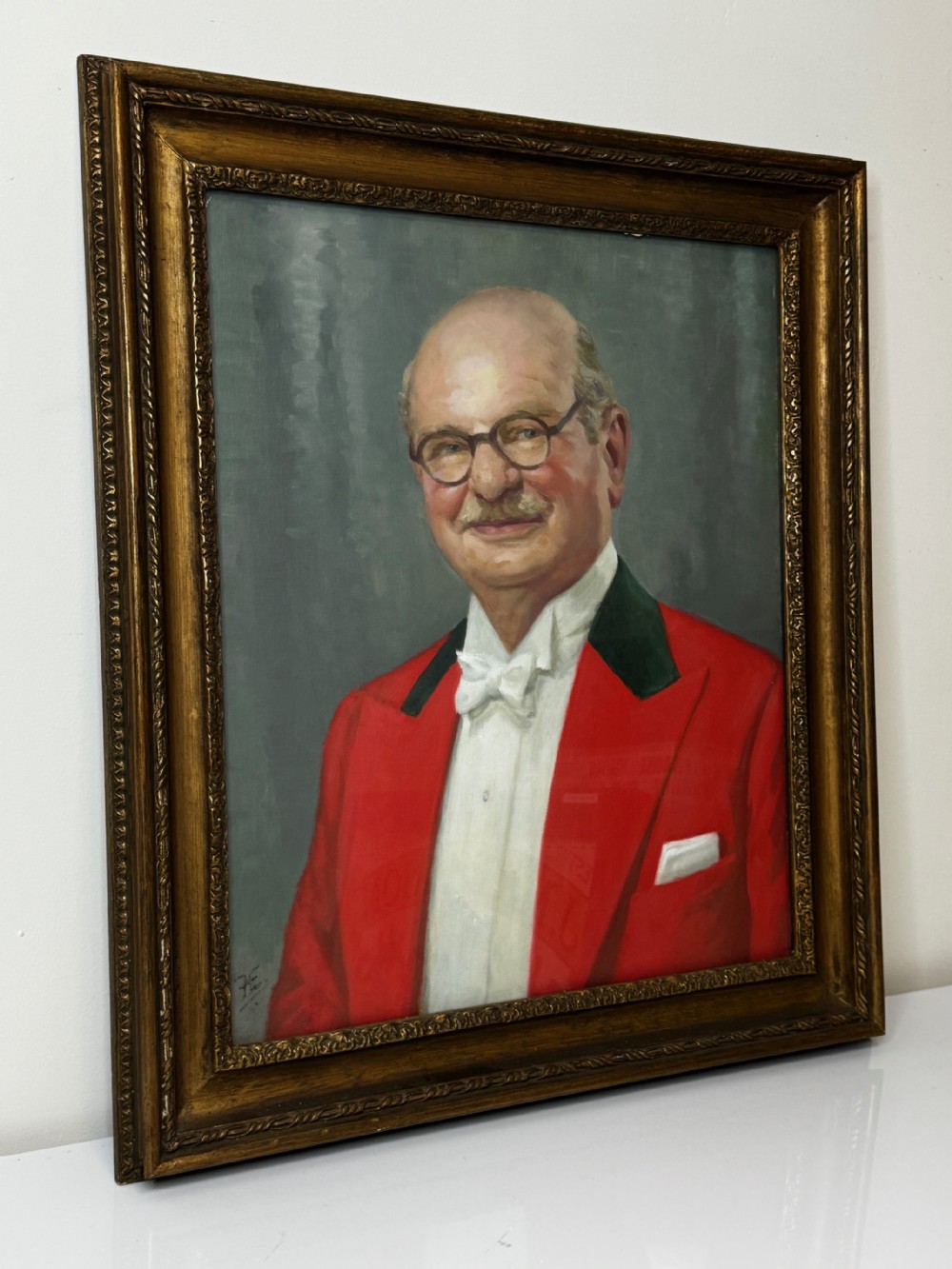 A mid-century oil painting depicting a gentleman wearing glasses, a red coat with dark lapels, and a white bow tie, housed within a gilded wooden frame. View II
