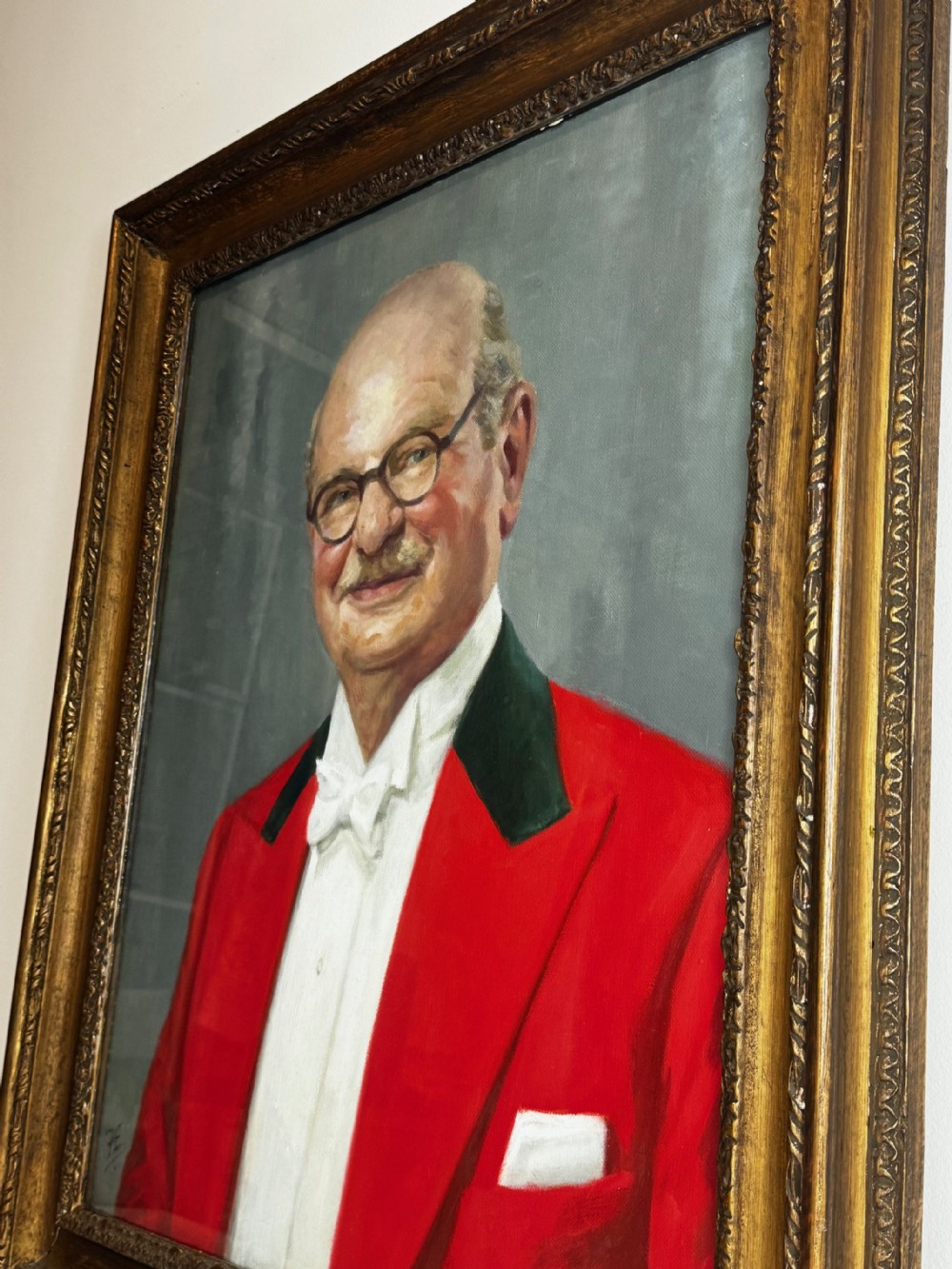 A mid-century oil painting depicting a gentleman wearing glasses, a red coat with dark lapels, and a white bow tie, housed within a gilded wooden frame. View III