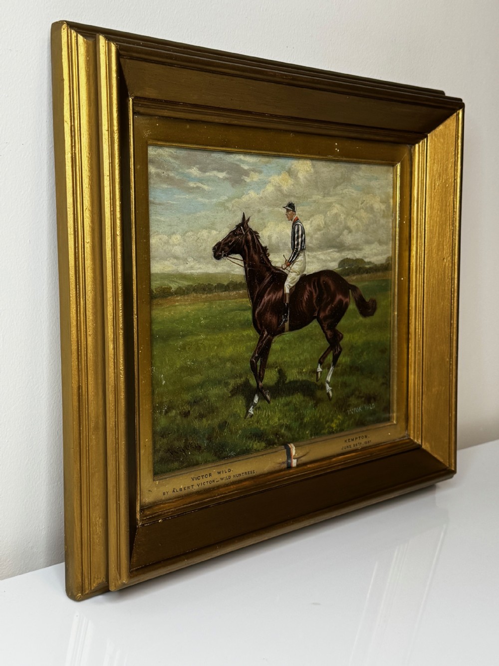 A Victorian equestrian oil painting set within a moulded gold gilt frame, depicting a brown racehorse and jockey in a field under a cloudy sky. View IX