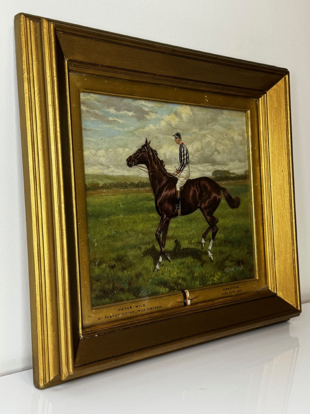 A Victorian equestrian oil painting set within a moulded gold gilt frame, depicting a brown racehorse and jockey in a field under a cloudy sky. View X