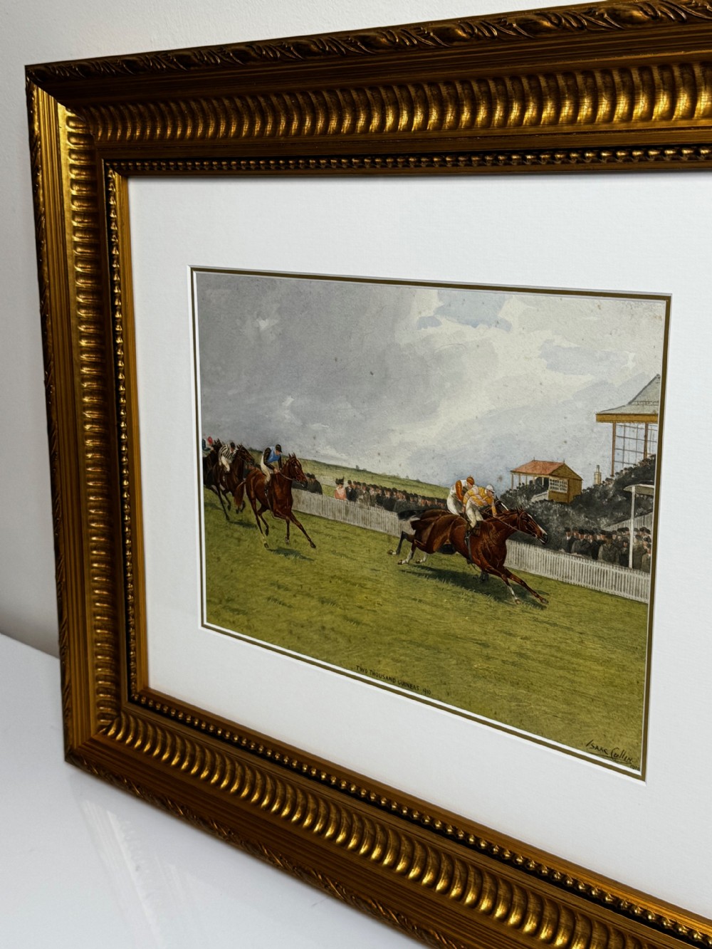 A framed British equestrian painting depicting racehorses and jockeys galloping on a green racetrack at Newmarket within a fluted gold-gilt frame. View VI