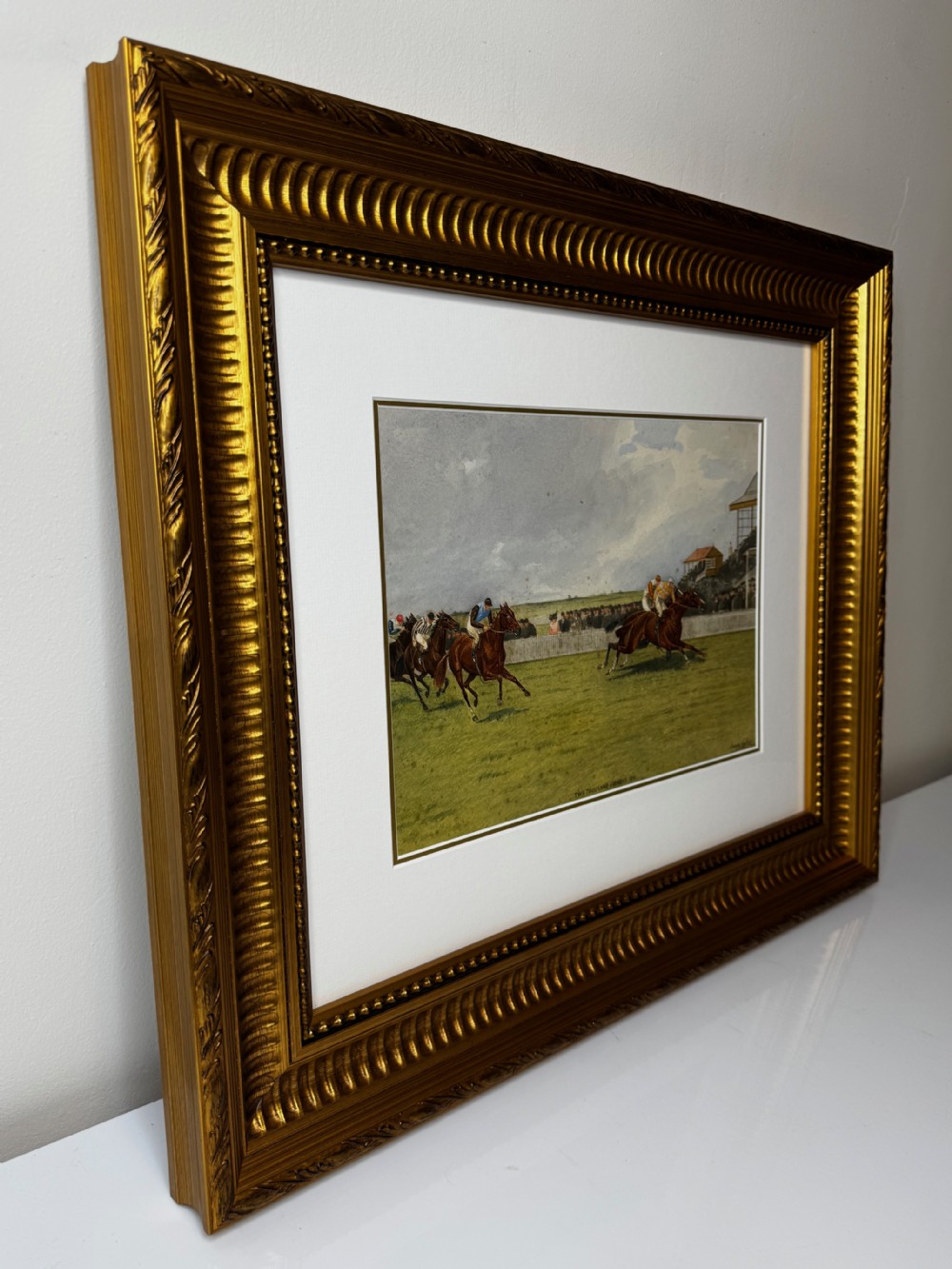 A framed British equestrian painting depicting racehorses and jockeys galloping on a green racetrack at Newmarket within a fluted gold-gilt frame. View XIII