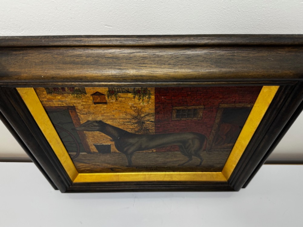 A Victorian oil painting depicting a dark brown greyhound standing in profile within a courtyard, presented in a dark molded wooden frame with a gold slip. View VI