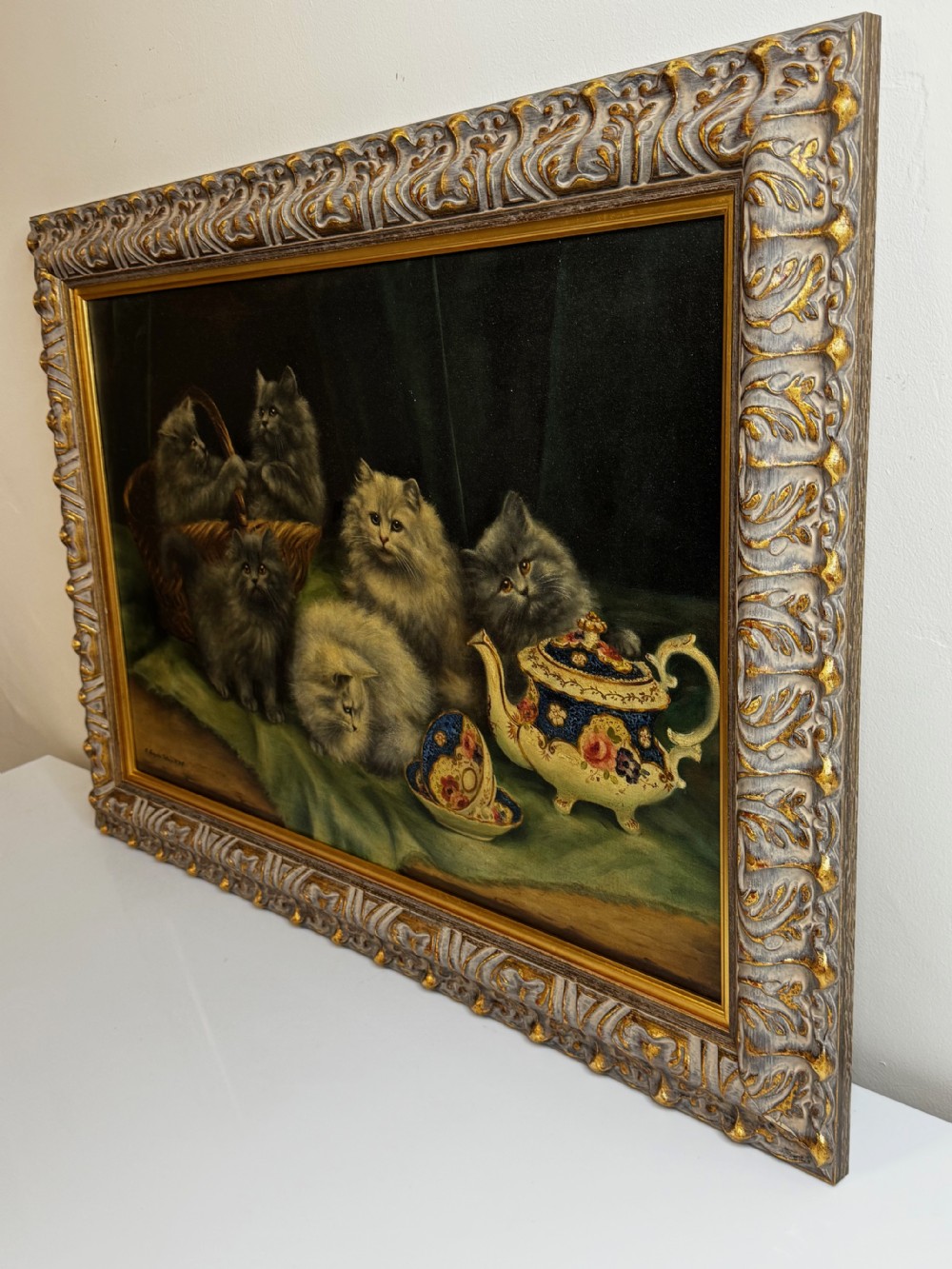 A framed oil painting featuring six fluffy grey and silver Persian kittens arranged around a woven basket and a decorated porcelain teapot. View V