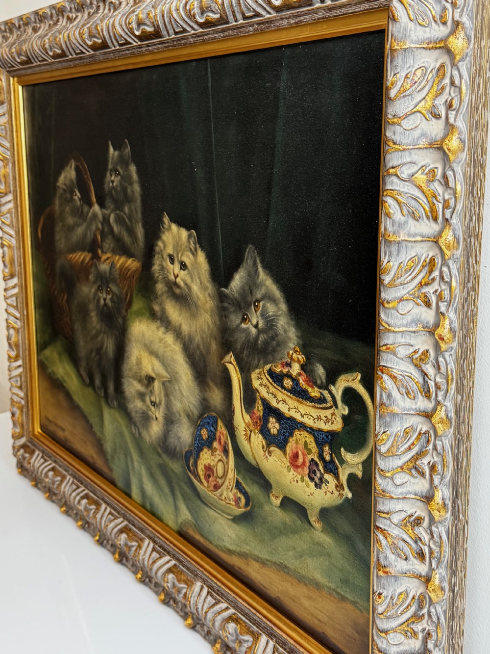 A framed oil painting featuring six fluffy grey and silver Persian kittens arranged around a woven basket and a decorated porcelain teapot. View VII