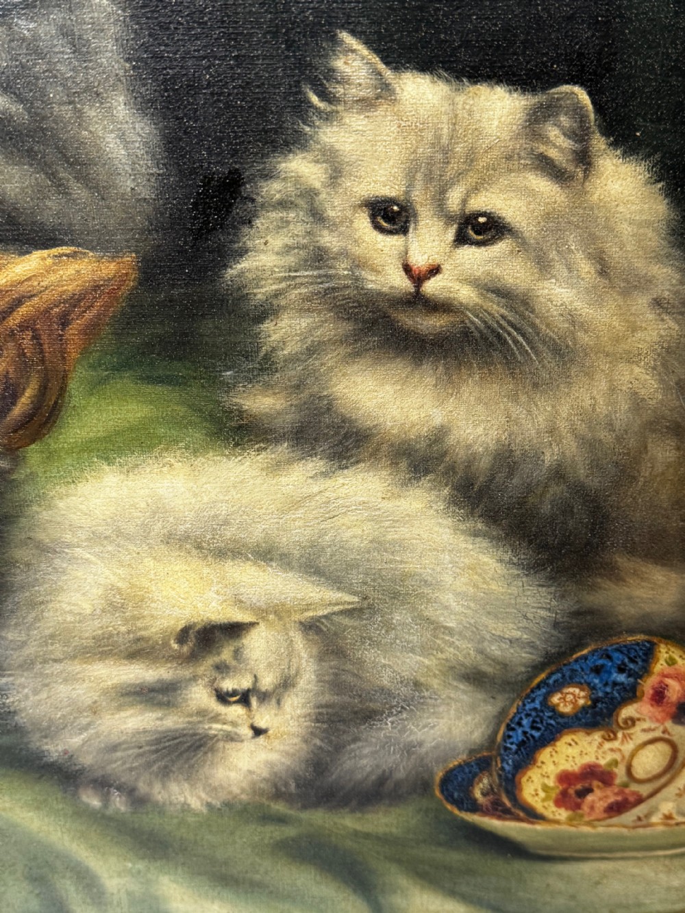 A framed oil painting featuring six fluffy grey and silver Persian kittens arranged around a woven basket and a decorated porcelain teapot. View XXII