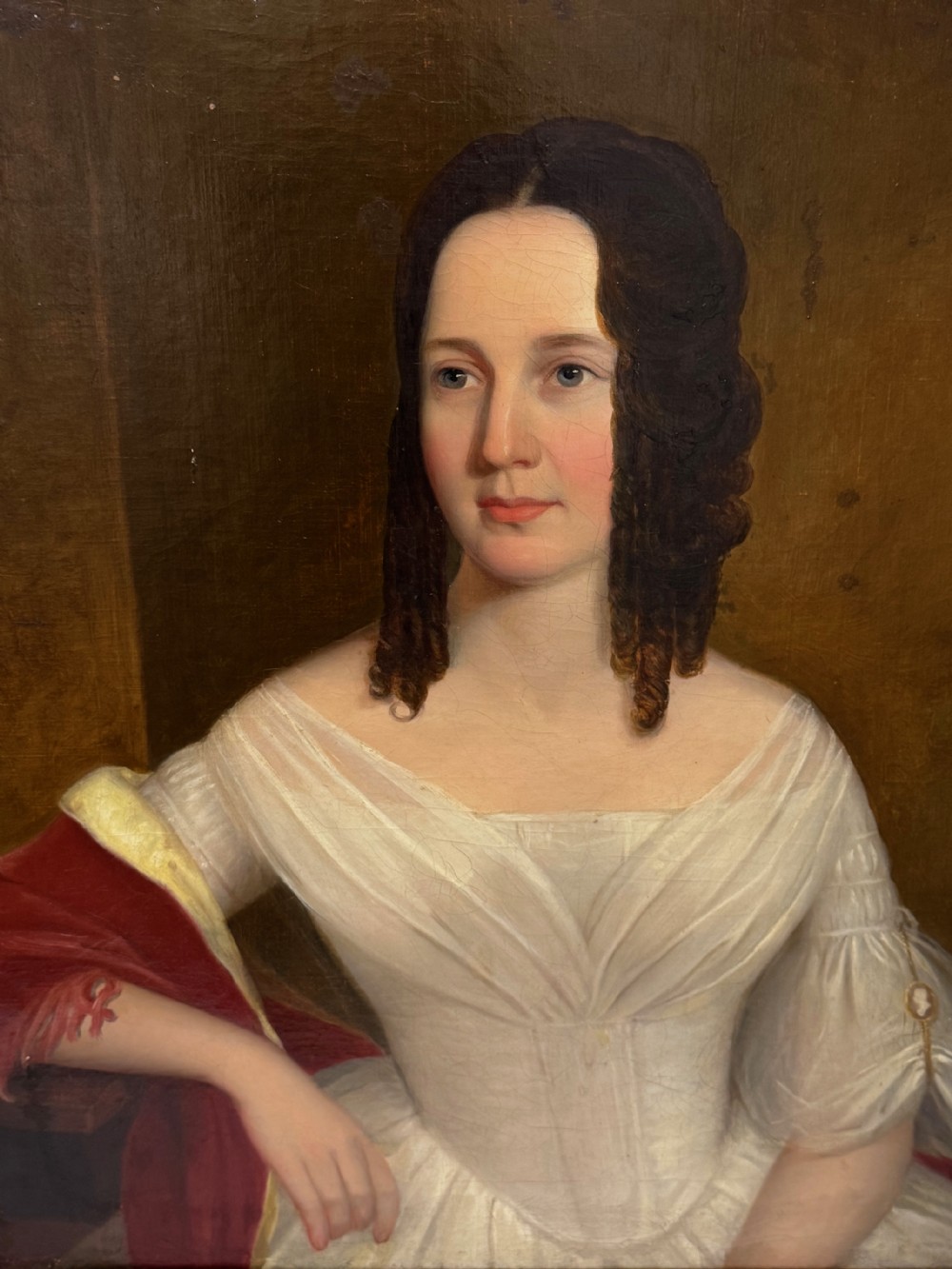 An antique Georgian oil portrait painting depicting a woman in a white off-the-shoulder gown with a red drape, framed in a beaded gold gilt frame. View XIII