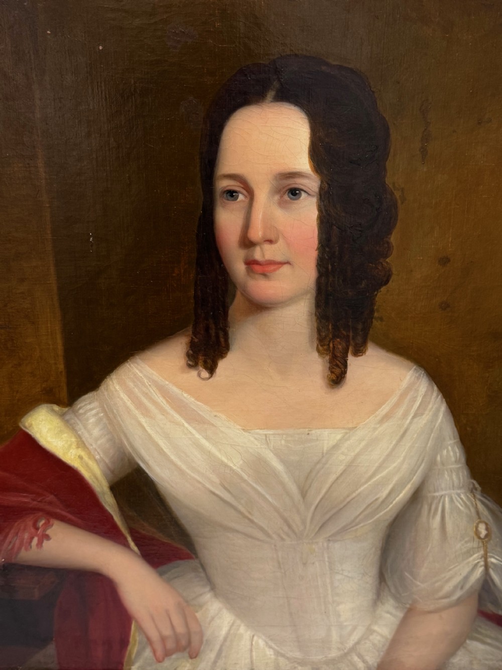An antique Georgian oil portrait painting depicting a woman in a white off-the-shoulder gown with a red drape, framed in a beaded gold gilt frame. View XIV
