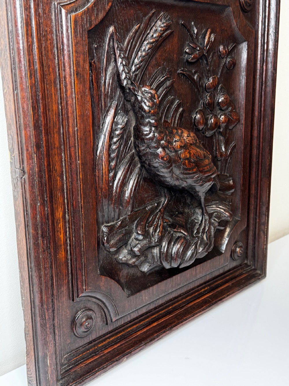 A dark oak relief carving depicting a game bird standing among reeds and oak leaves with acorns inside a moulded frame. View III